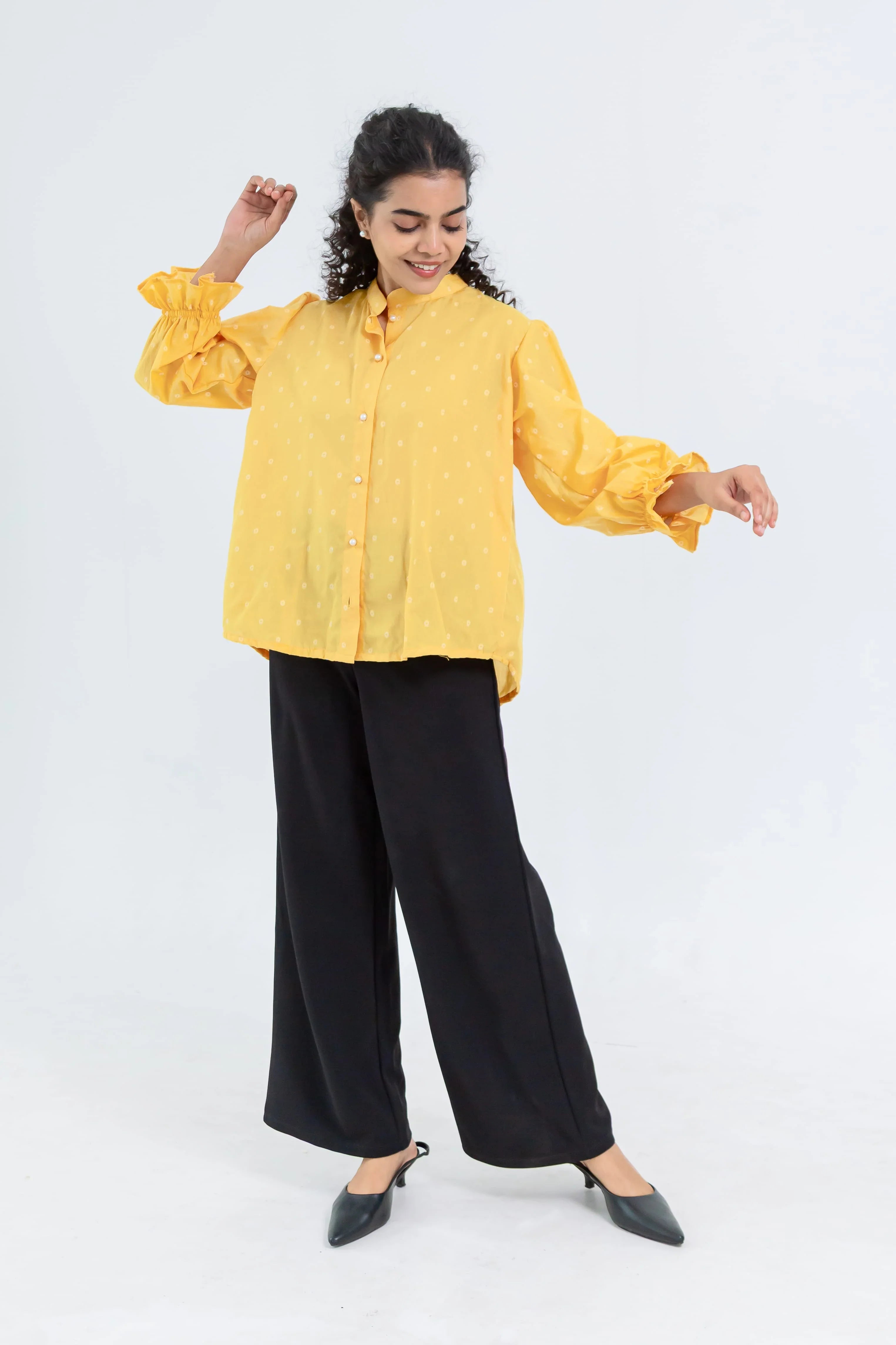 Woman in a yellow polka dot blouse with ruffle sleeves and black wide-leg pants