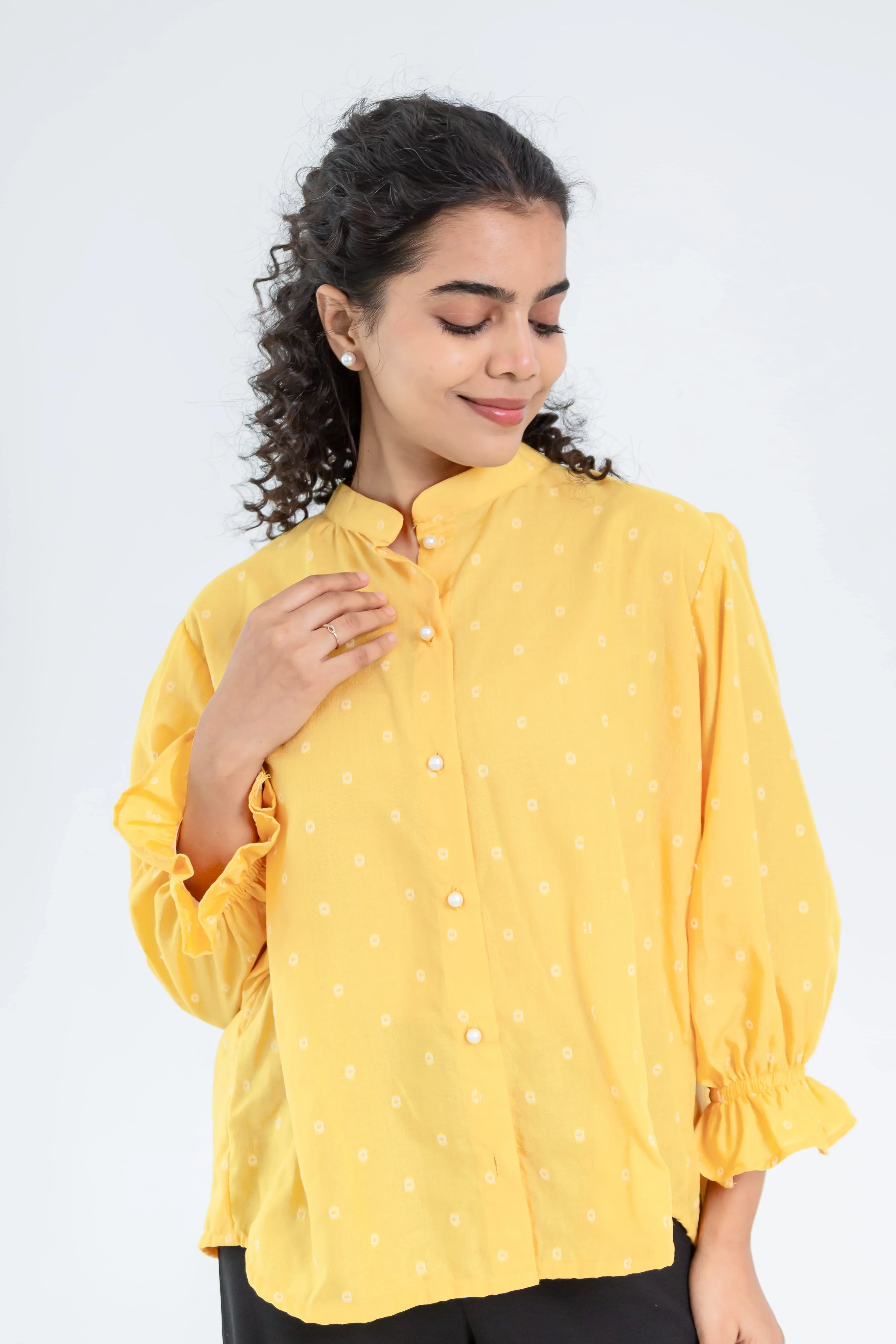 Woman wearing a loose-fit yellow button-down top with small white prints and bishop sleeves