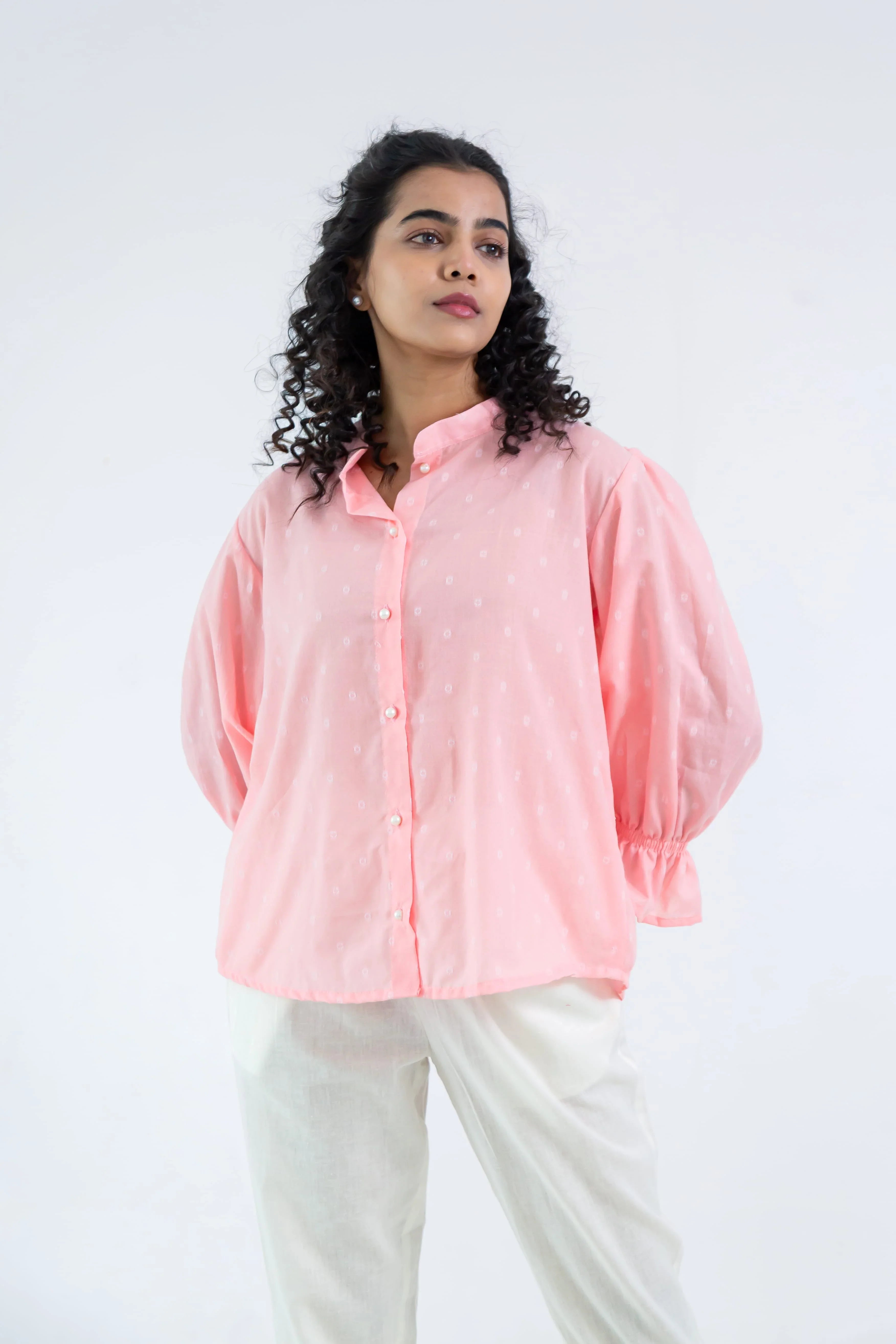 Woman wearing a loose pink button-up shirt with white prints and white trousers