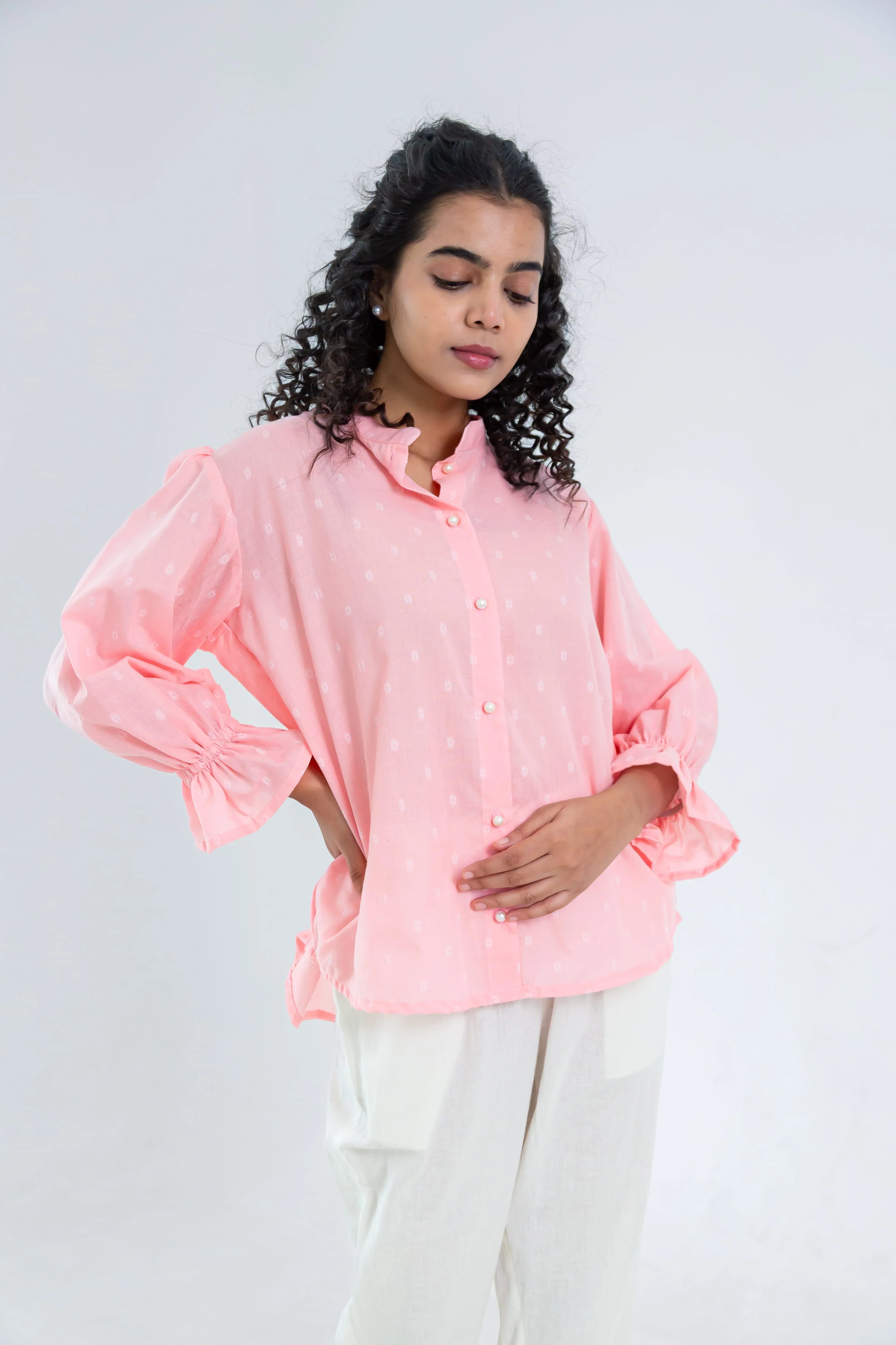 Woman wearing a light pink button-up top with puff sleeves and off-white pants