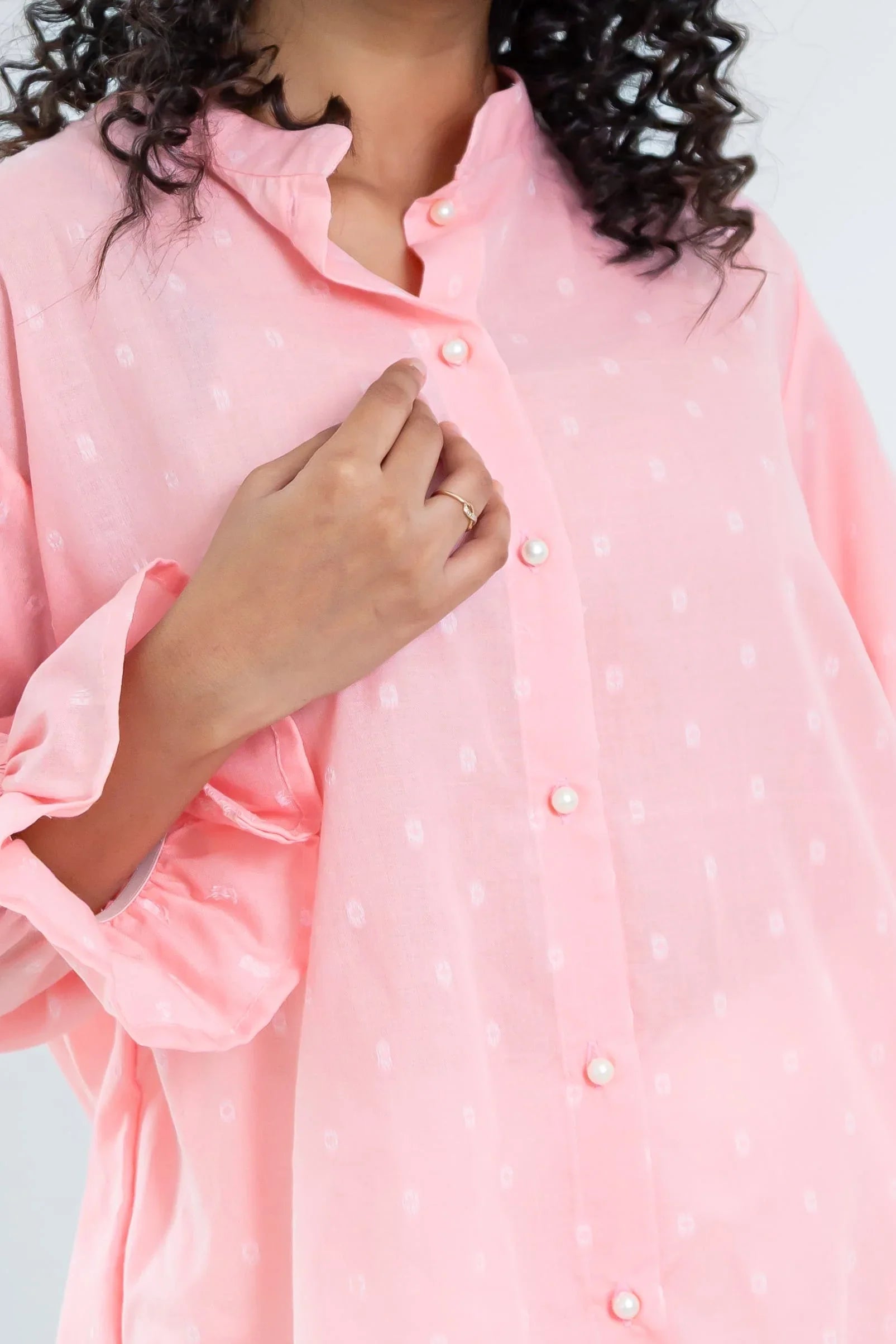 Close-up of woman wearing a light pink button-down dress with pearl buttons and subtle print