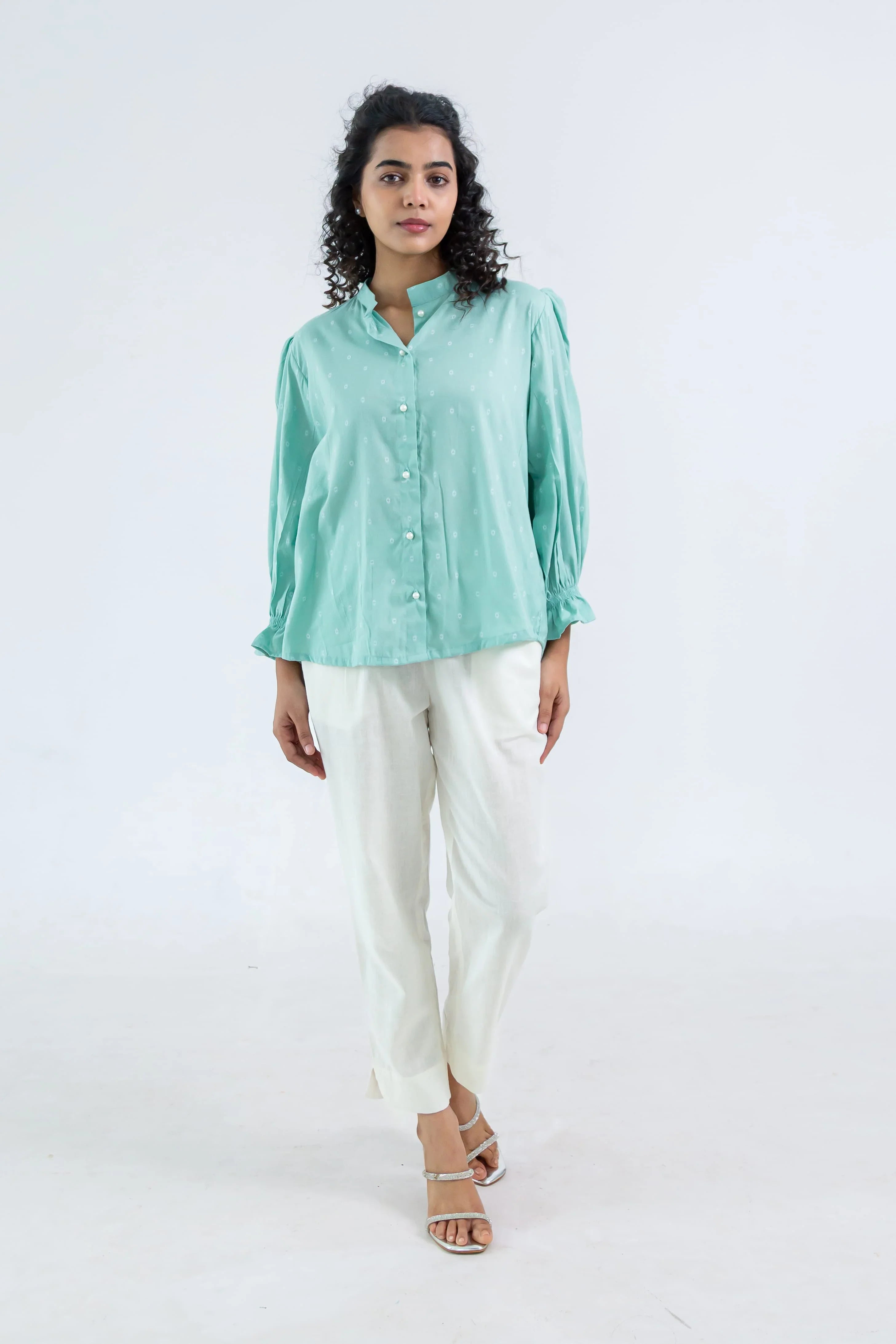 Woman wearing a mint green button-up top with puff sleeves and white straight pants