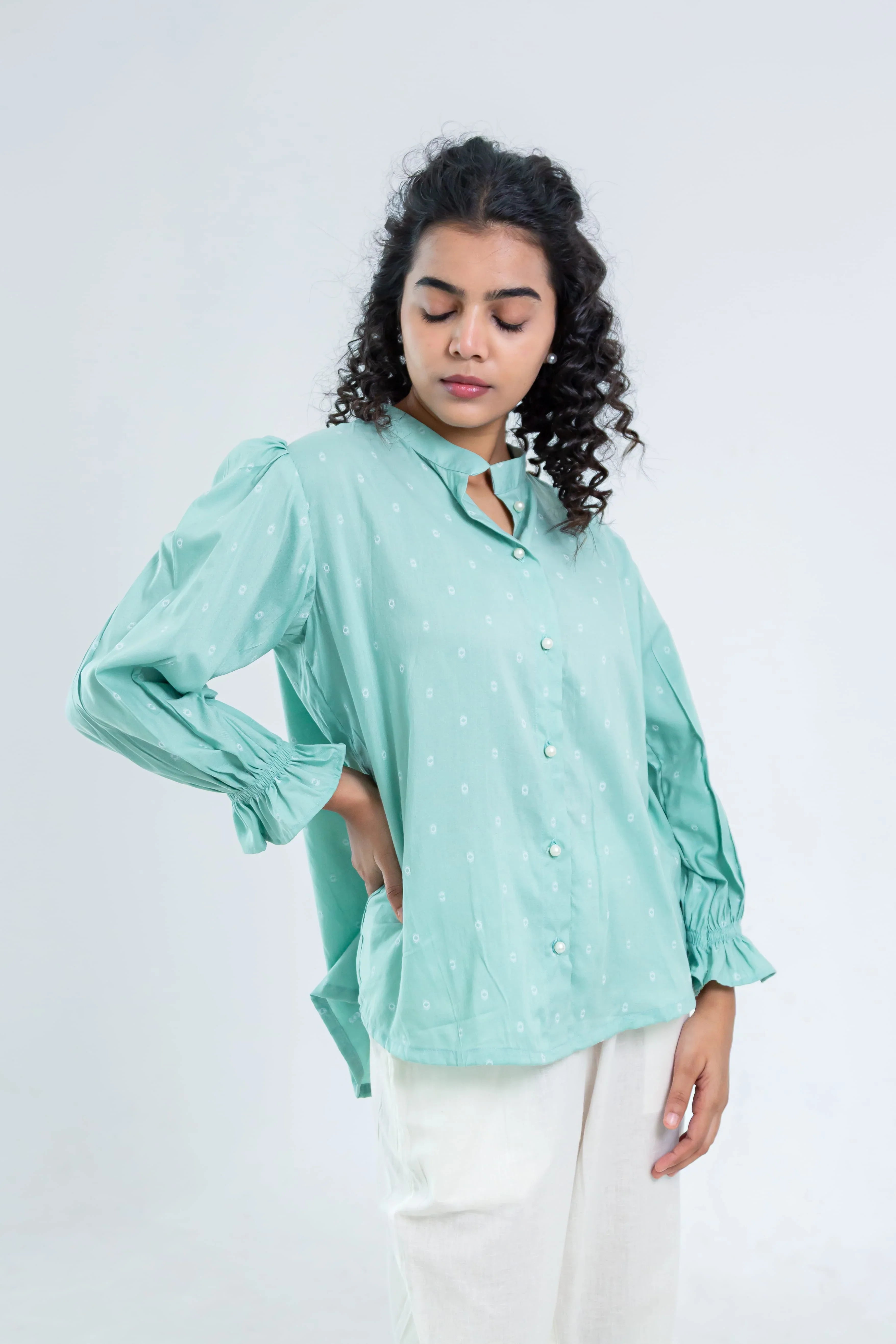 Woman wearing light green printed button-down shirt with puff sleeves and white pants