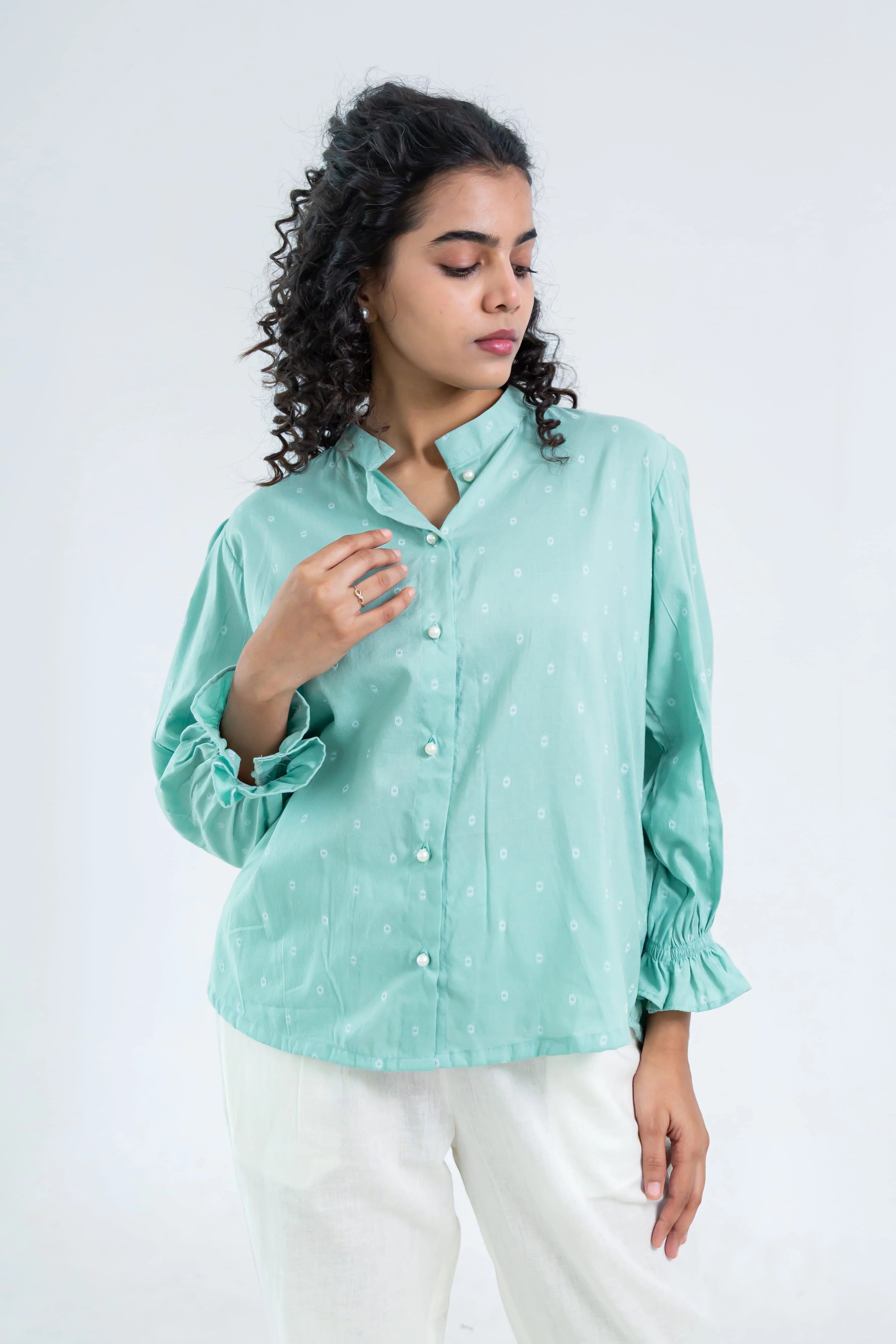 Woman wearing a mint green button-up shirt with subtle prints and white pants
