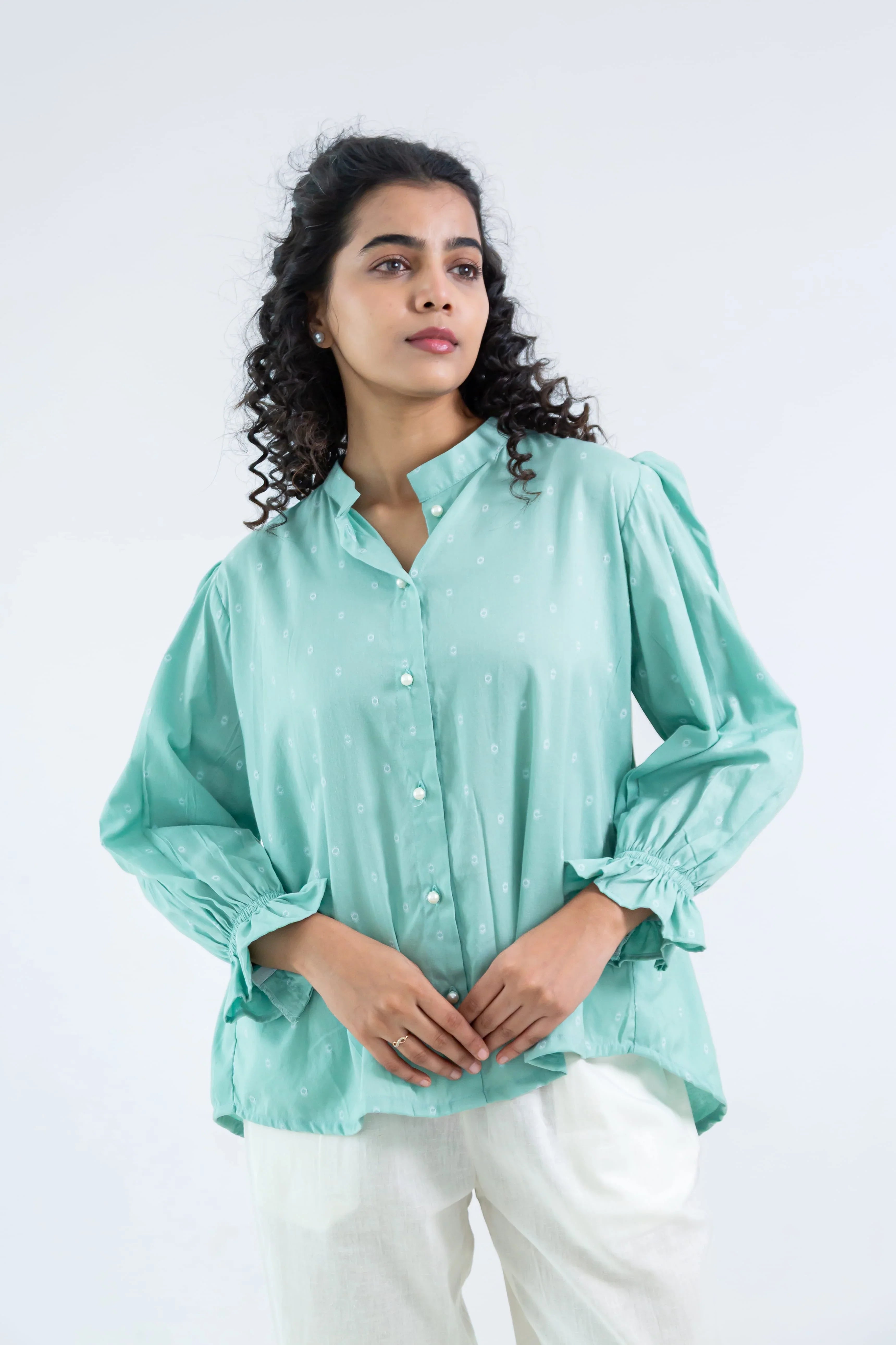 Woman in mint green button-up blouse with subtle print and white pants, minimalist background