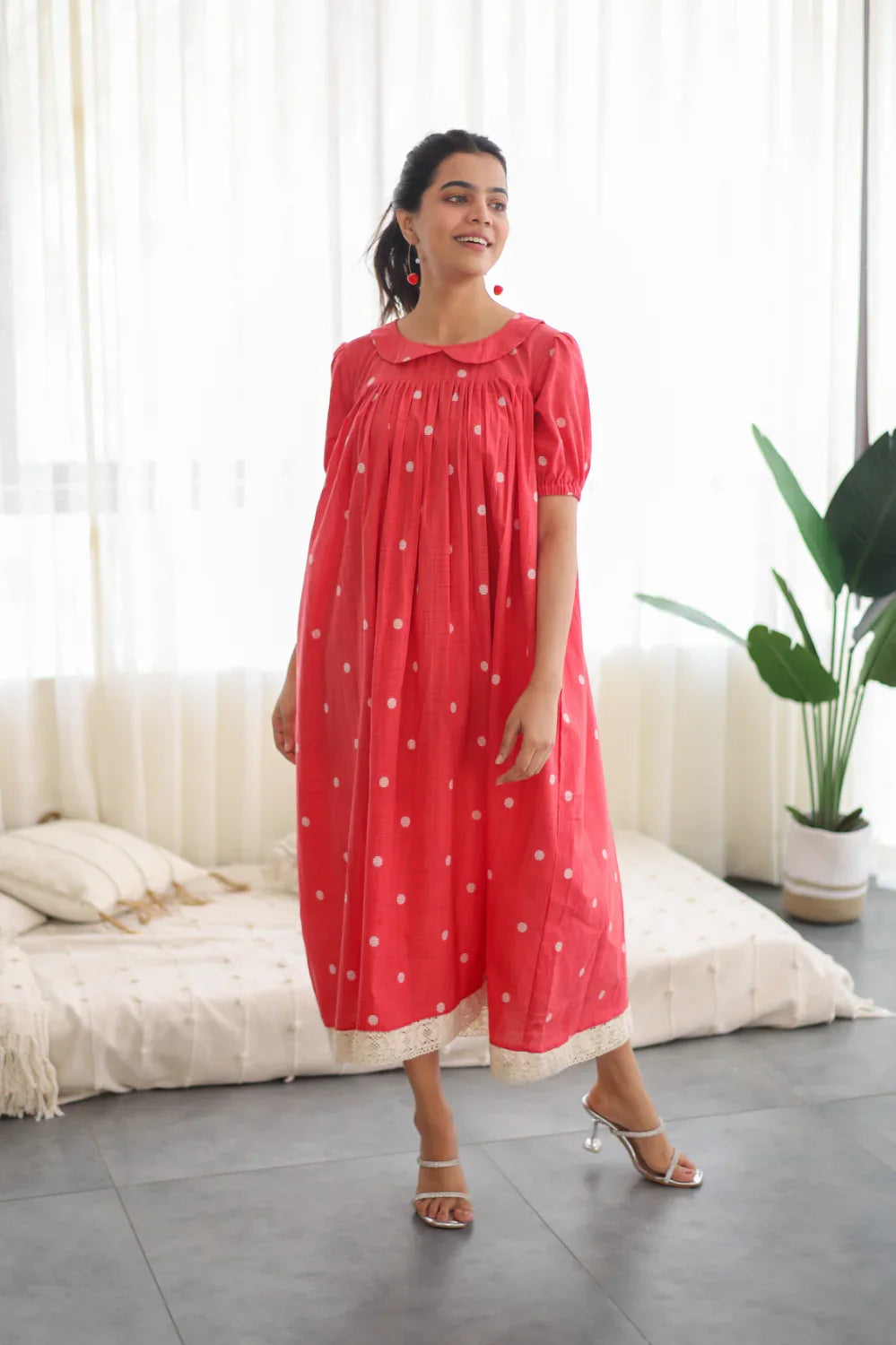 Woman wearing a red polka dot midi dress with puff sleeves and lace hem, casual indoor setting