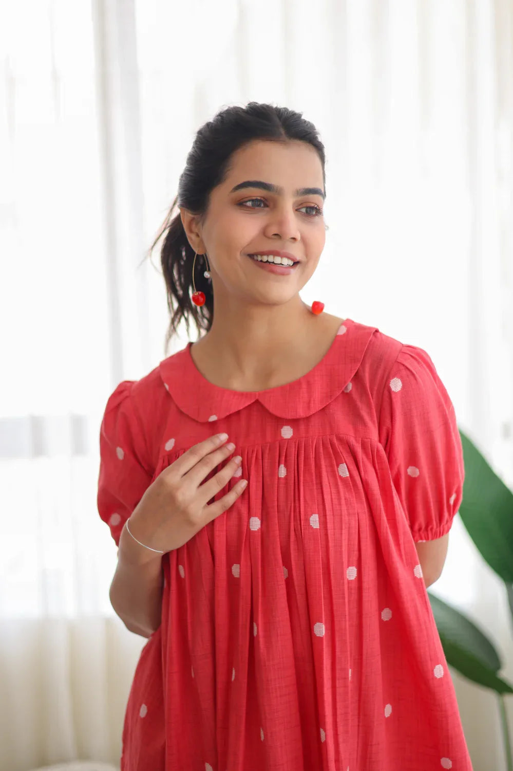 Woman in a pink polka dot dress with puff sleeves, standing indoors and smiling