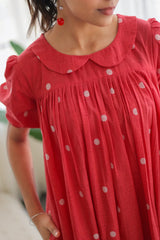 Woman wearing a red polka dot dress with puff sleeves and a scalloped collar