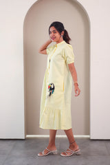 Woman in a light yellow midi dress with puff sleeves and toucan embroidery, posing indoors