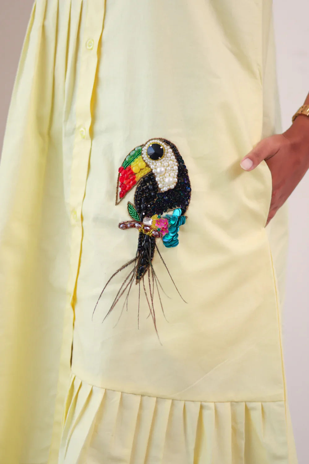 Yellow dress with hand in pocket featuring a colorful beaded toucan patch
