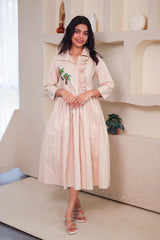 Woman wearing a beige midi dress with palm tree embroidery and ruffle details indoors