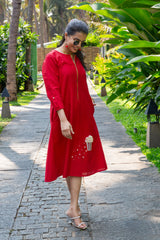 Woman in a red midi dress with pearl embellishments, walking outdoors on a sunny path