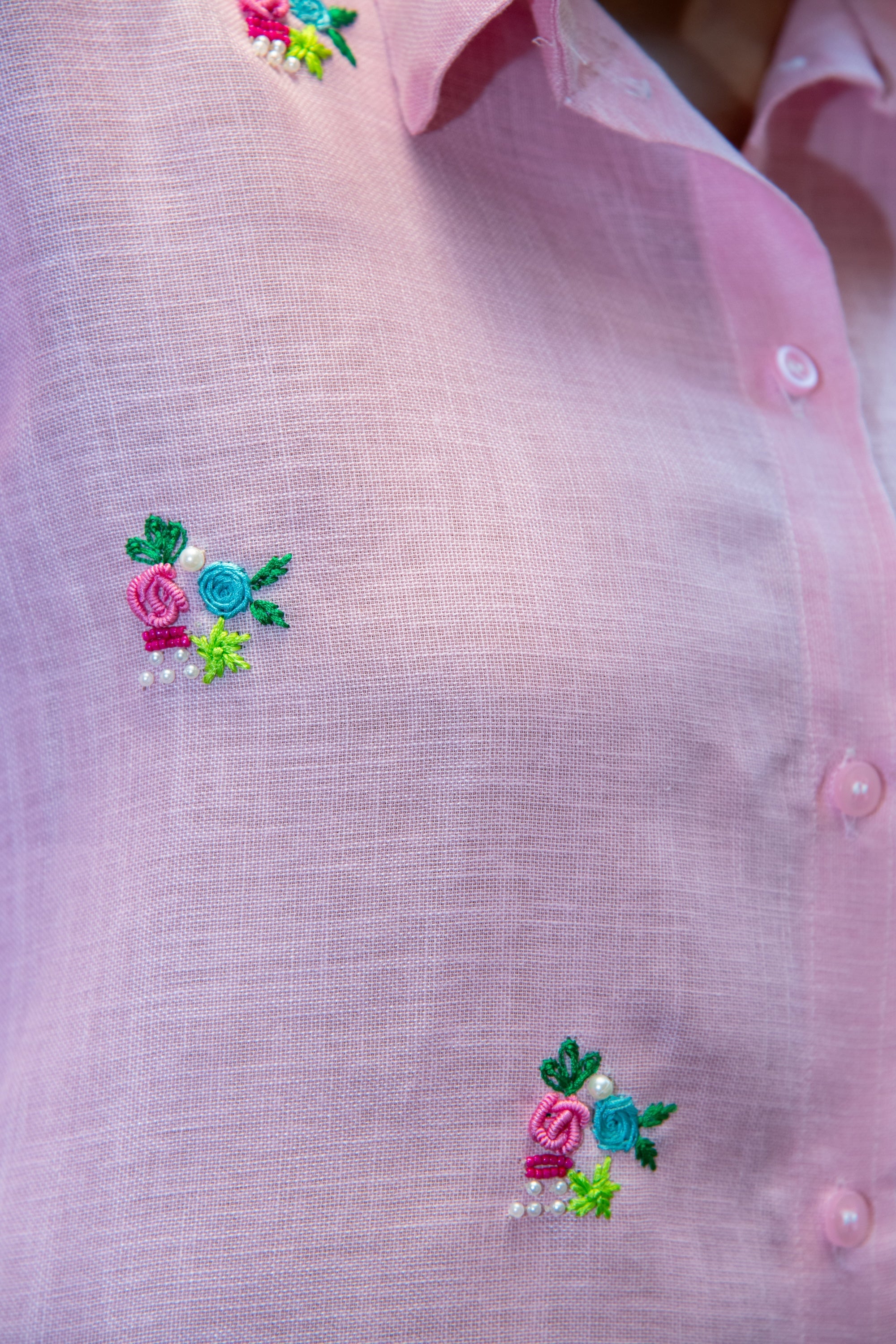 Pink shirt with colorful floral embroidery and pearl accents, featuring vibrant roses and green leaves.