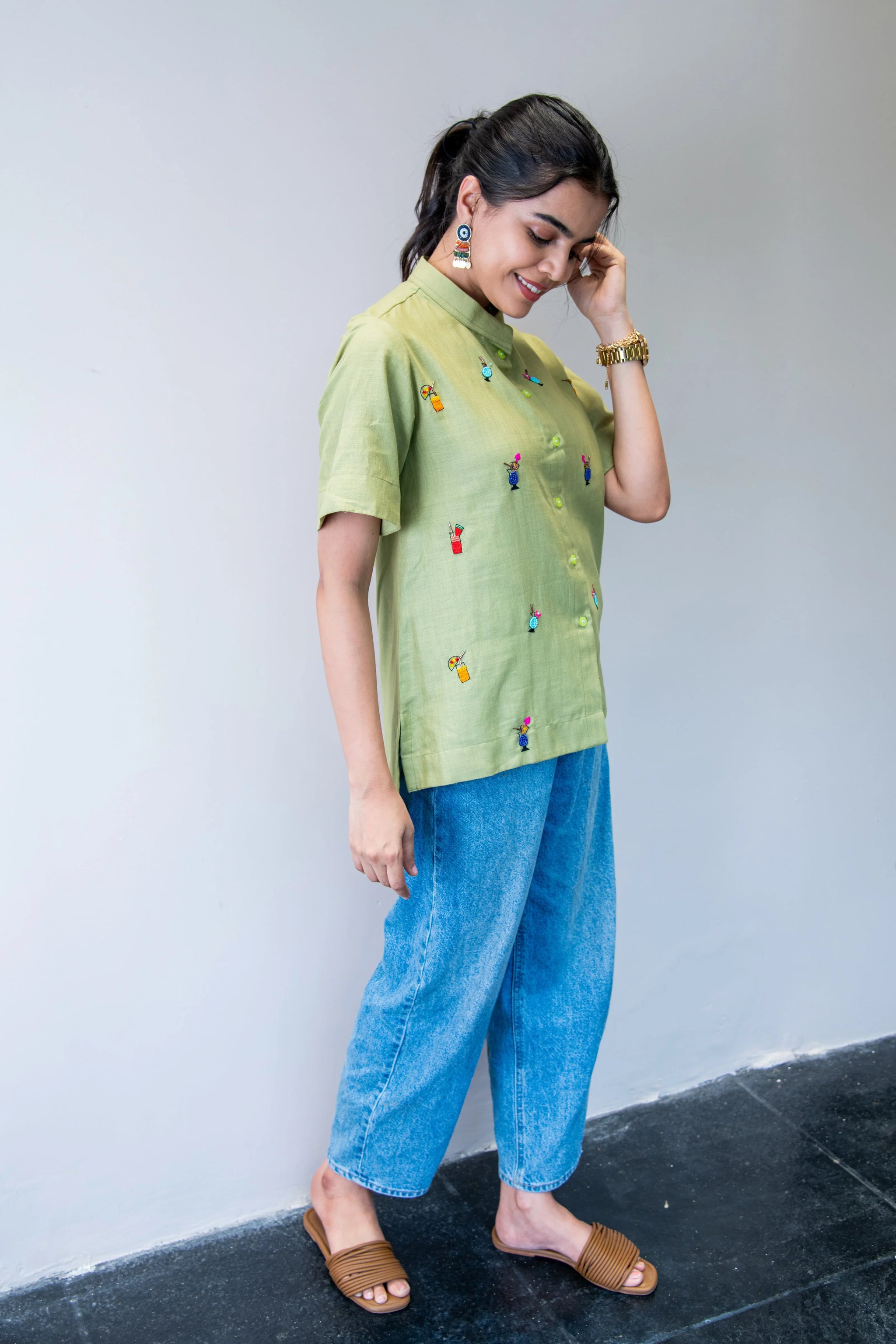 Woman in a light green embroidered shirt and blue jeans, wearing slide sandals