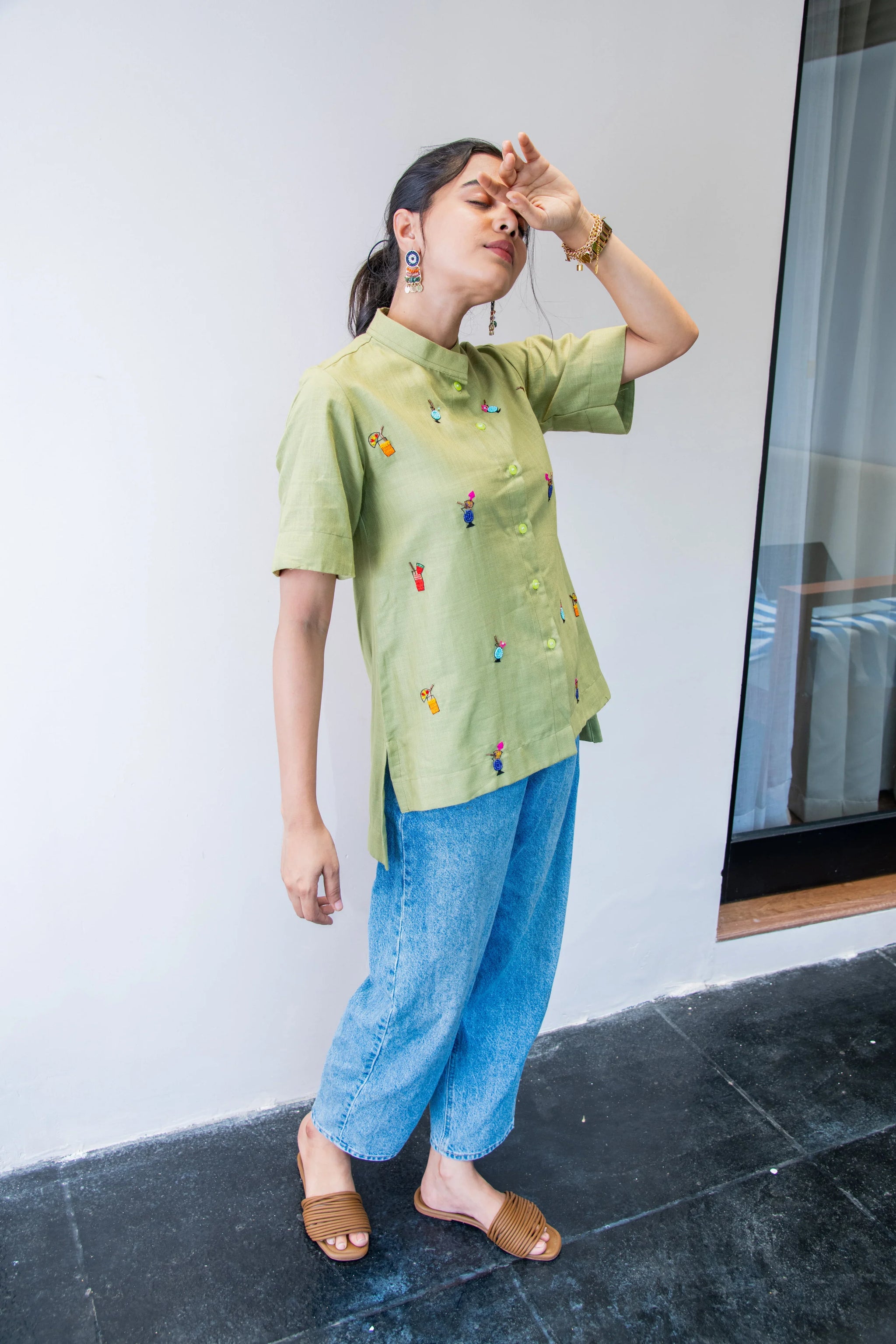 Woman in green embroidered shirt and blue jeans posing indoors, casual trendy outfit