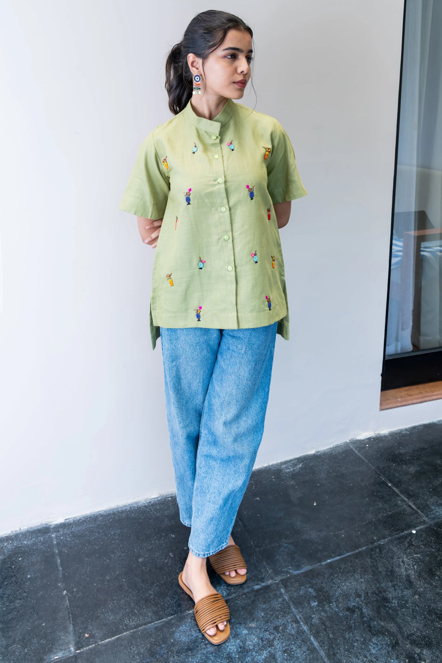 Woman wearing a light green embroidered shirt with blue jeans and brown sandals