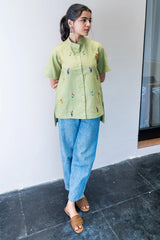 Woman wearing a light green embroidered shirt with blue jeans and brown sandals