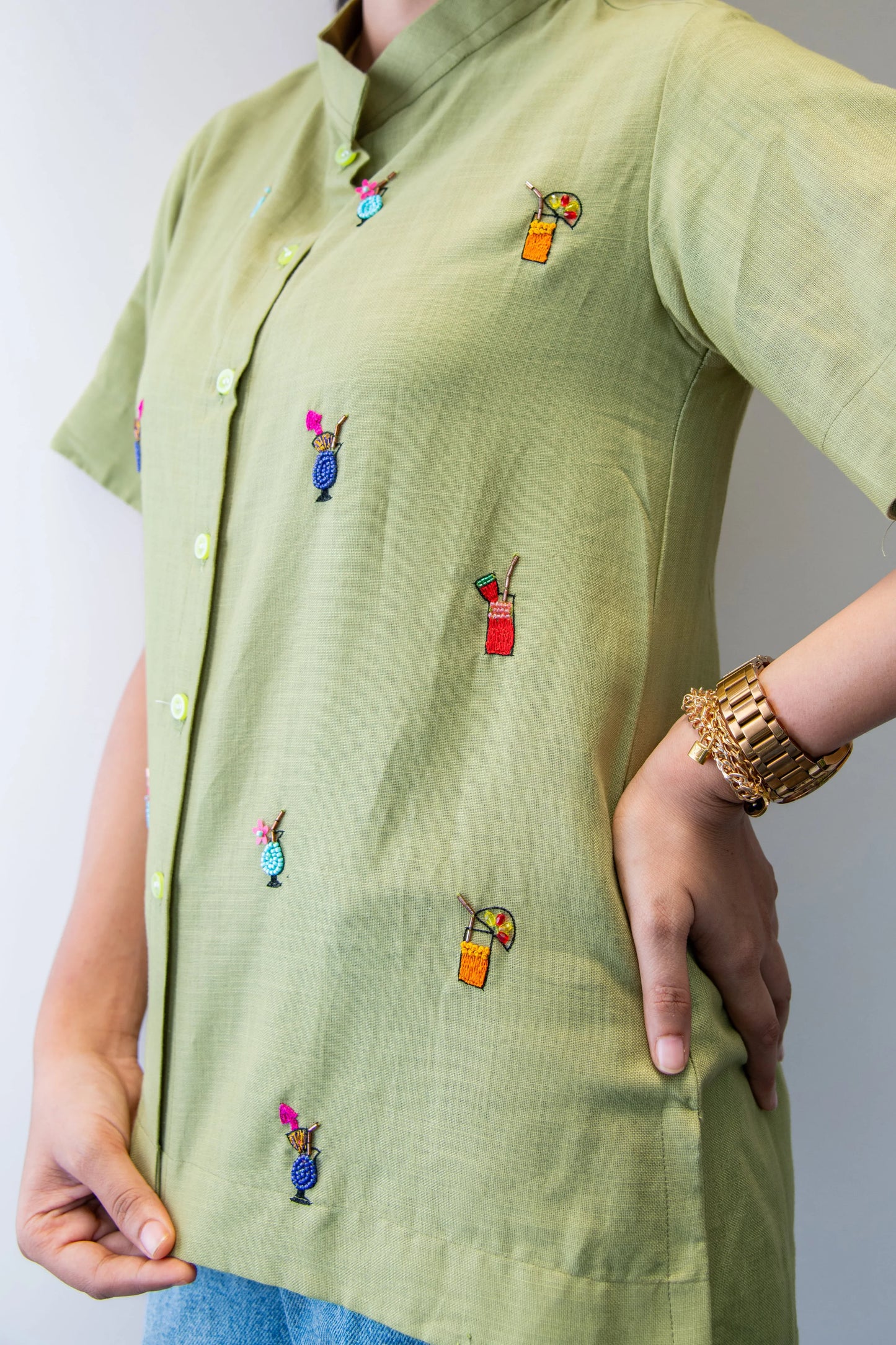 Light green short-sleeved shirt with colorful drink embroidery, gold watch on wrist