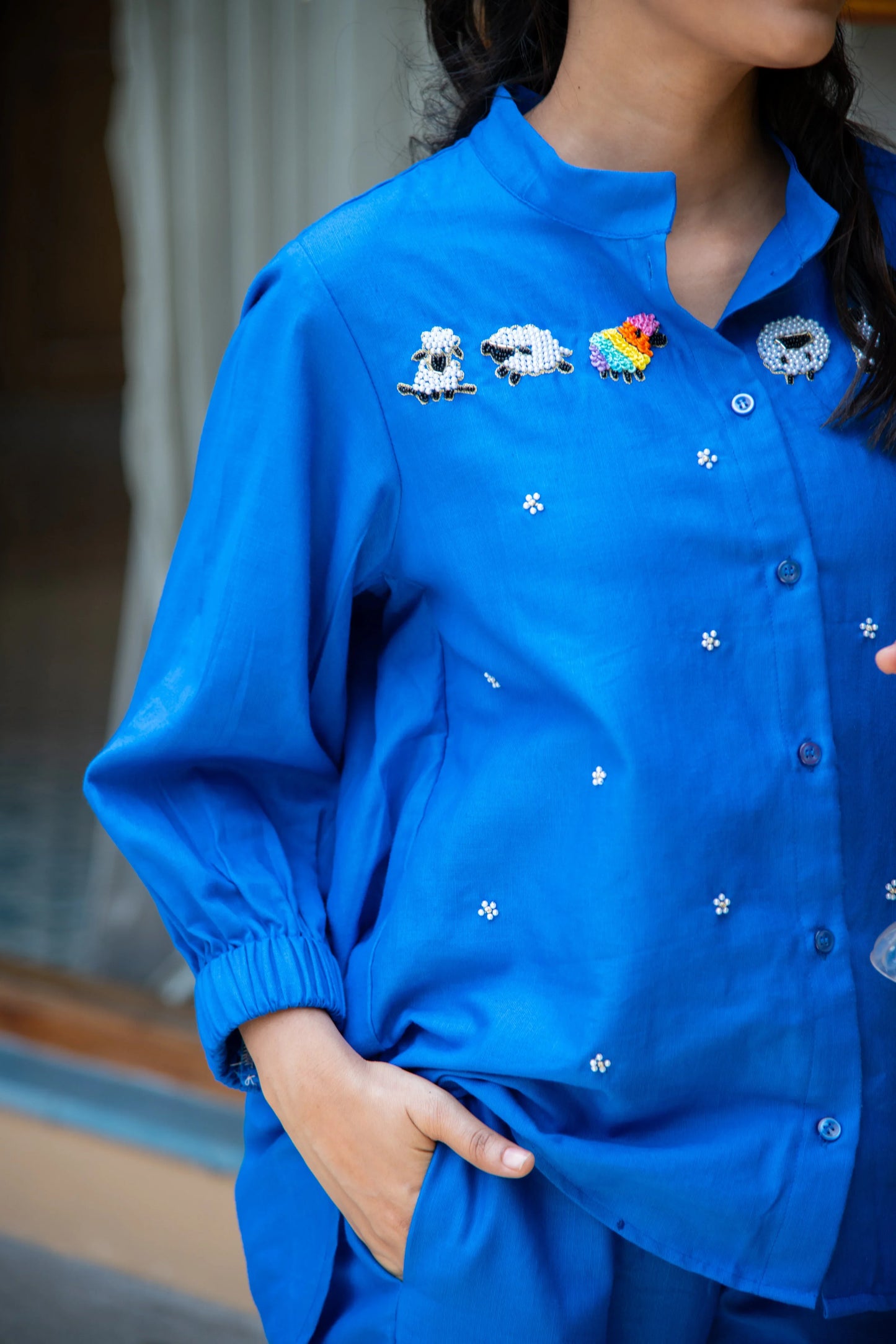 Woman in a bright blue shirt with embroidered sheep and small floral details