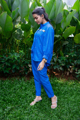 Woman in blue co-ord set with embellished shirt, standing outdoors on grass