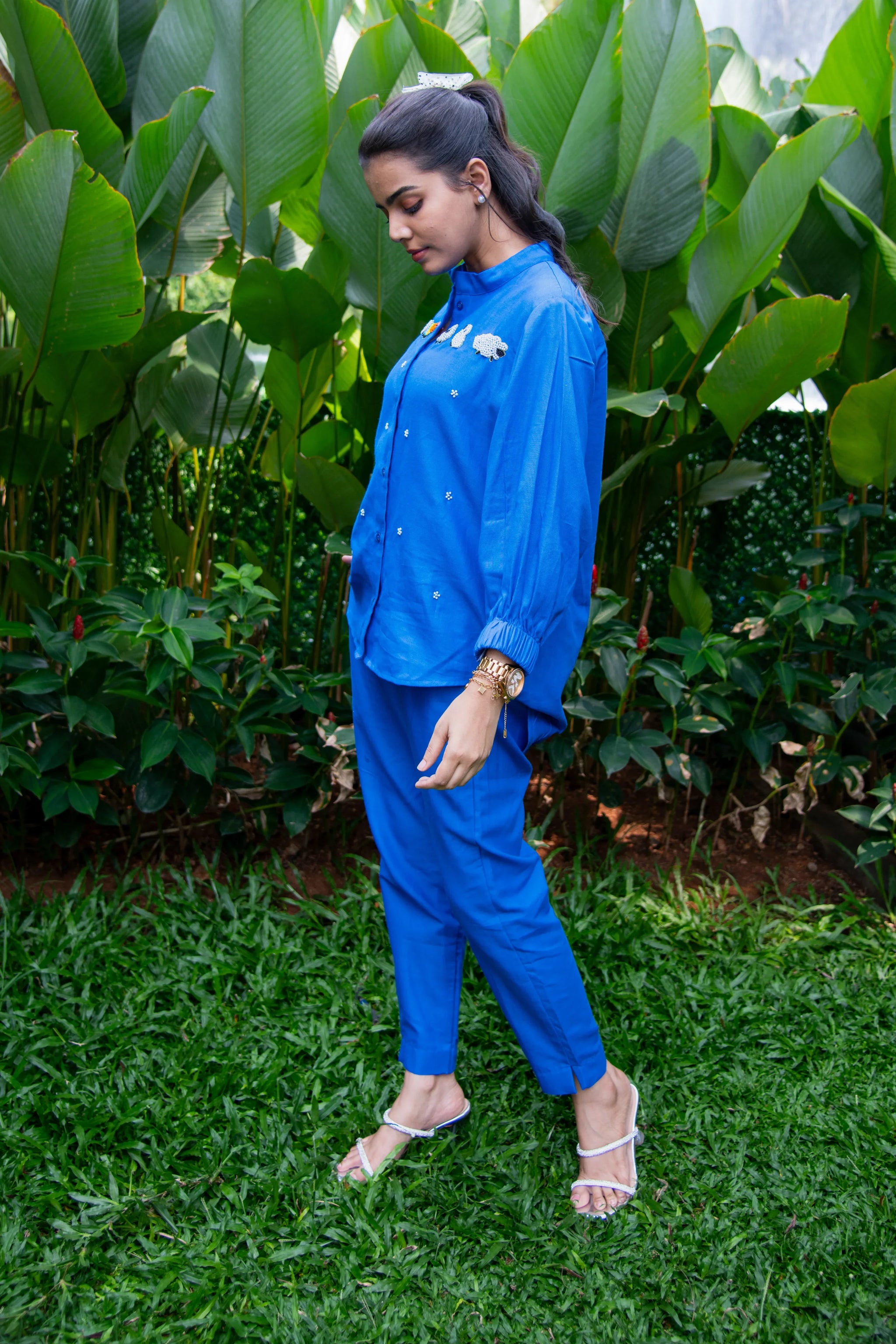 Woman in blue co-ord set with embellished shirt, standing outdoors on grass