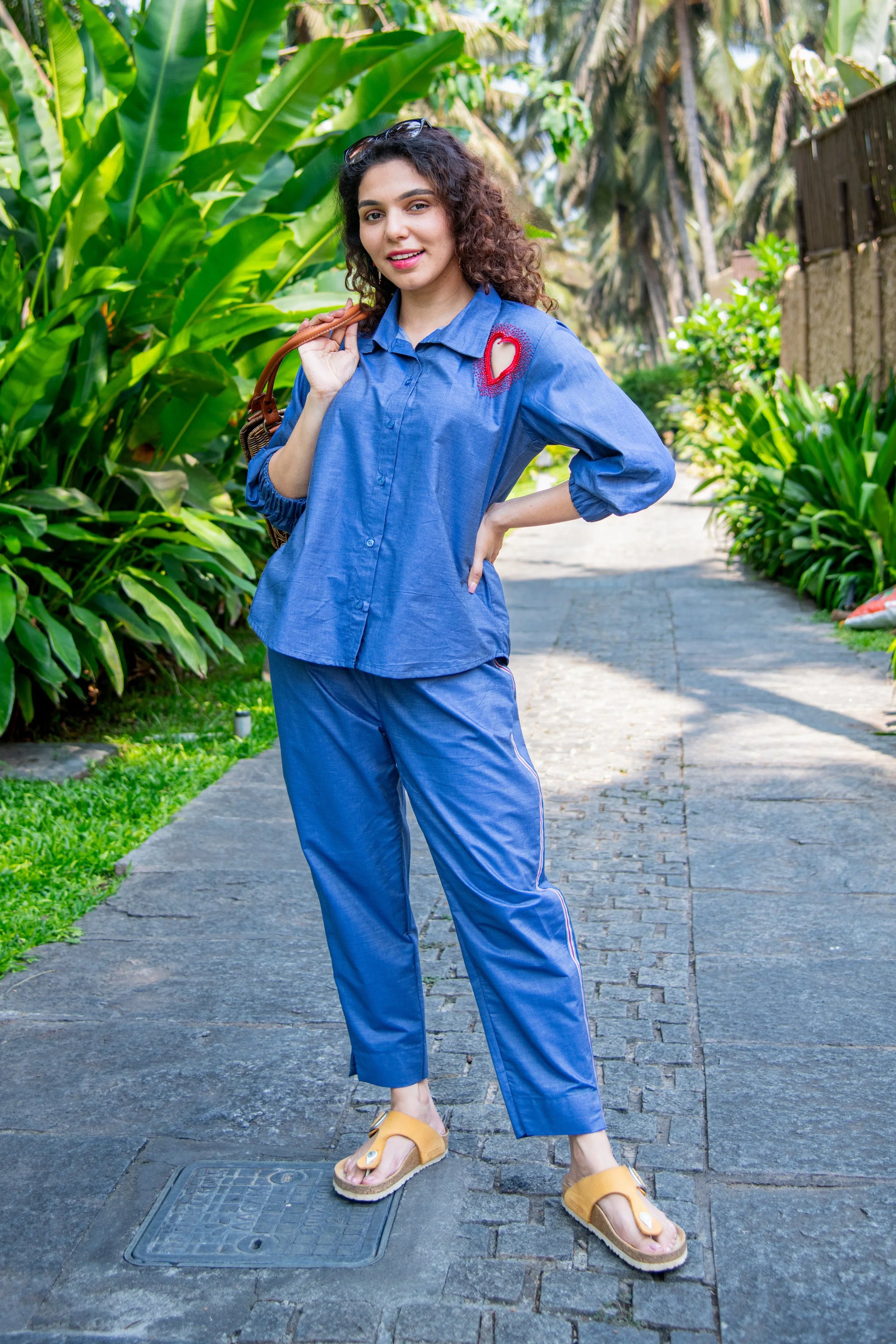 Woman in a blue co-ord set with red heart detail, standing outdoors on a leafy path