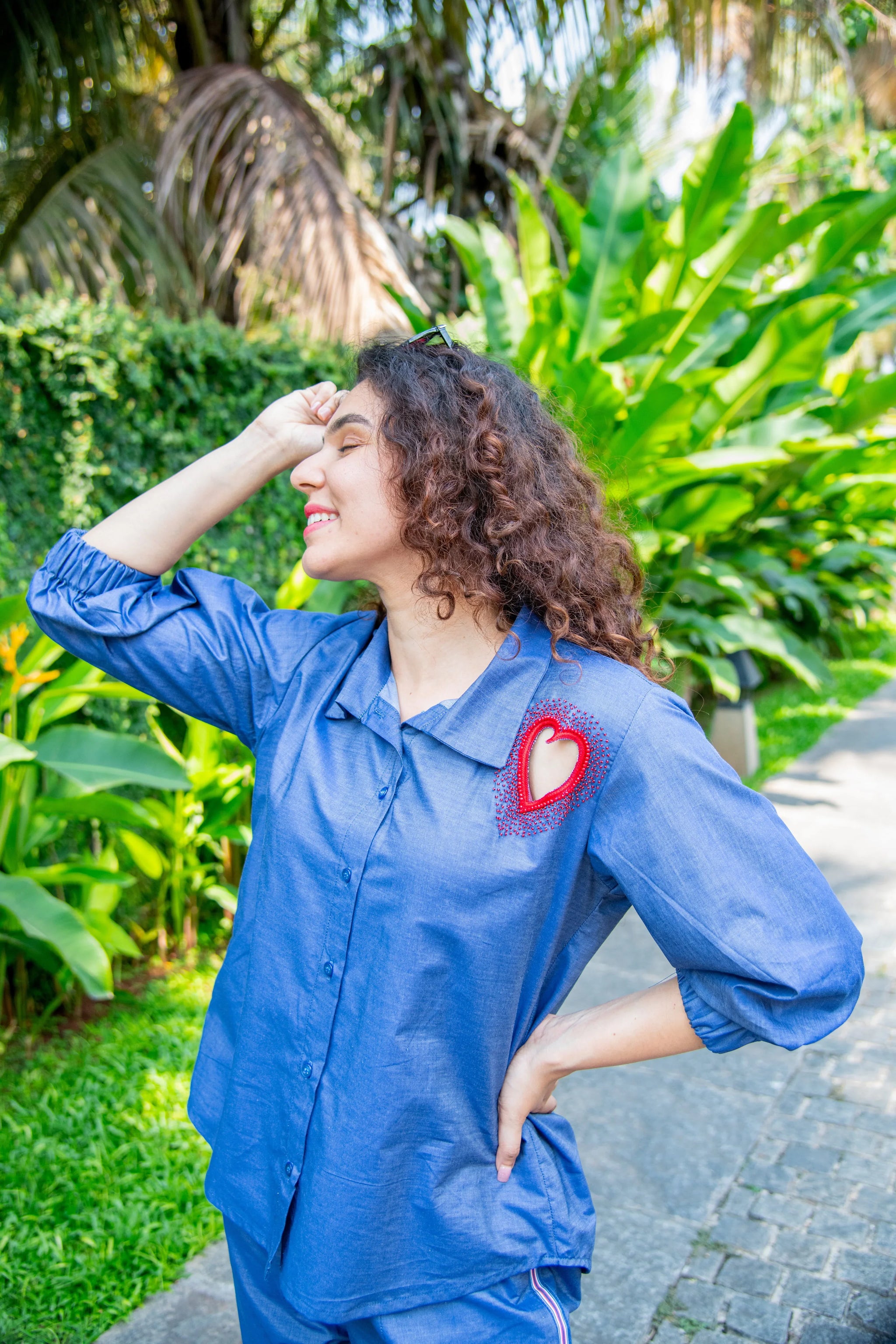 Woman in blue co-ord set with red heart cutout detail, posing outdoors among green plants