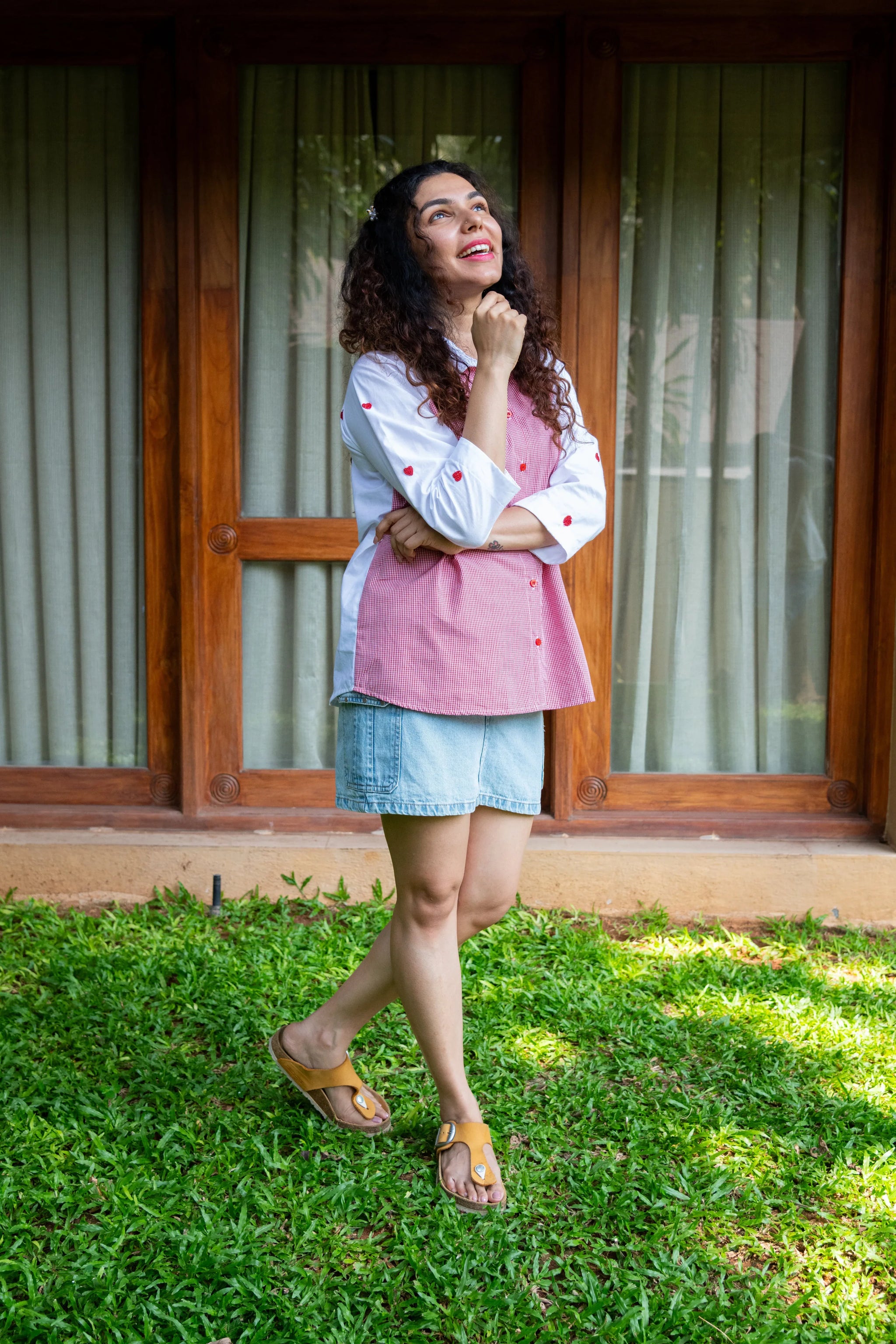Woman in casual red and white shirt with heart print, denim shorts, and sandals standing on grass