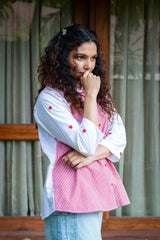 Woman in pink gingham top with red heart embroidery and light blue jeans, outdoors