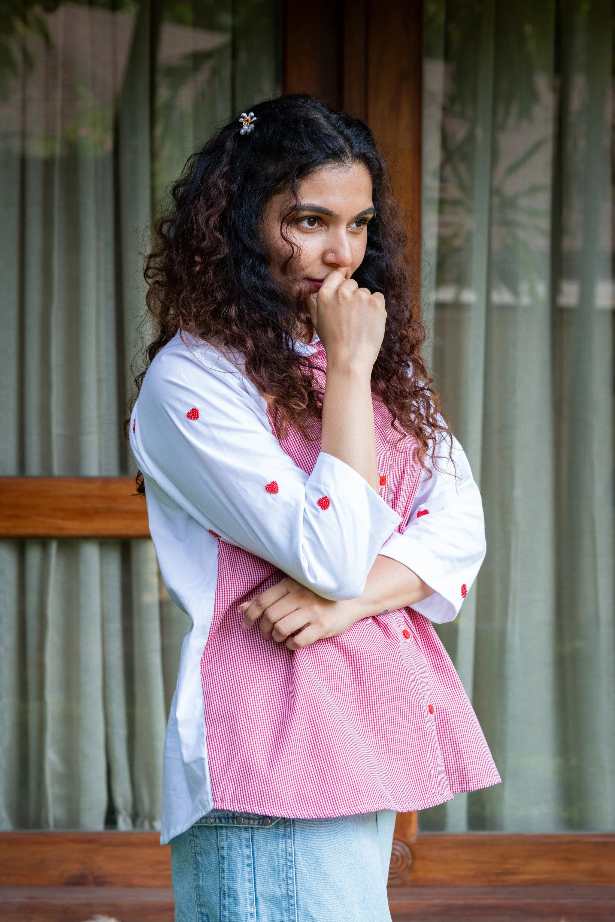 Woman in pink gingham top with red heart embroidery and light blue jeans, outdoors
