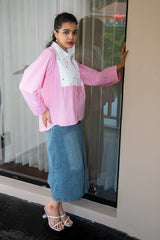Woman in a pink long sleeve shirt and denim midi skirt posing by a glass door