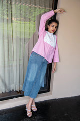 Woman in pink and white shirt with embroidery, blue denim skirt, and heeled sandals posing outdoors
