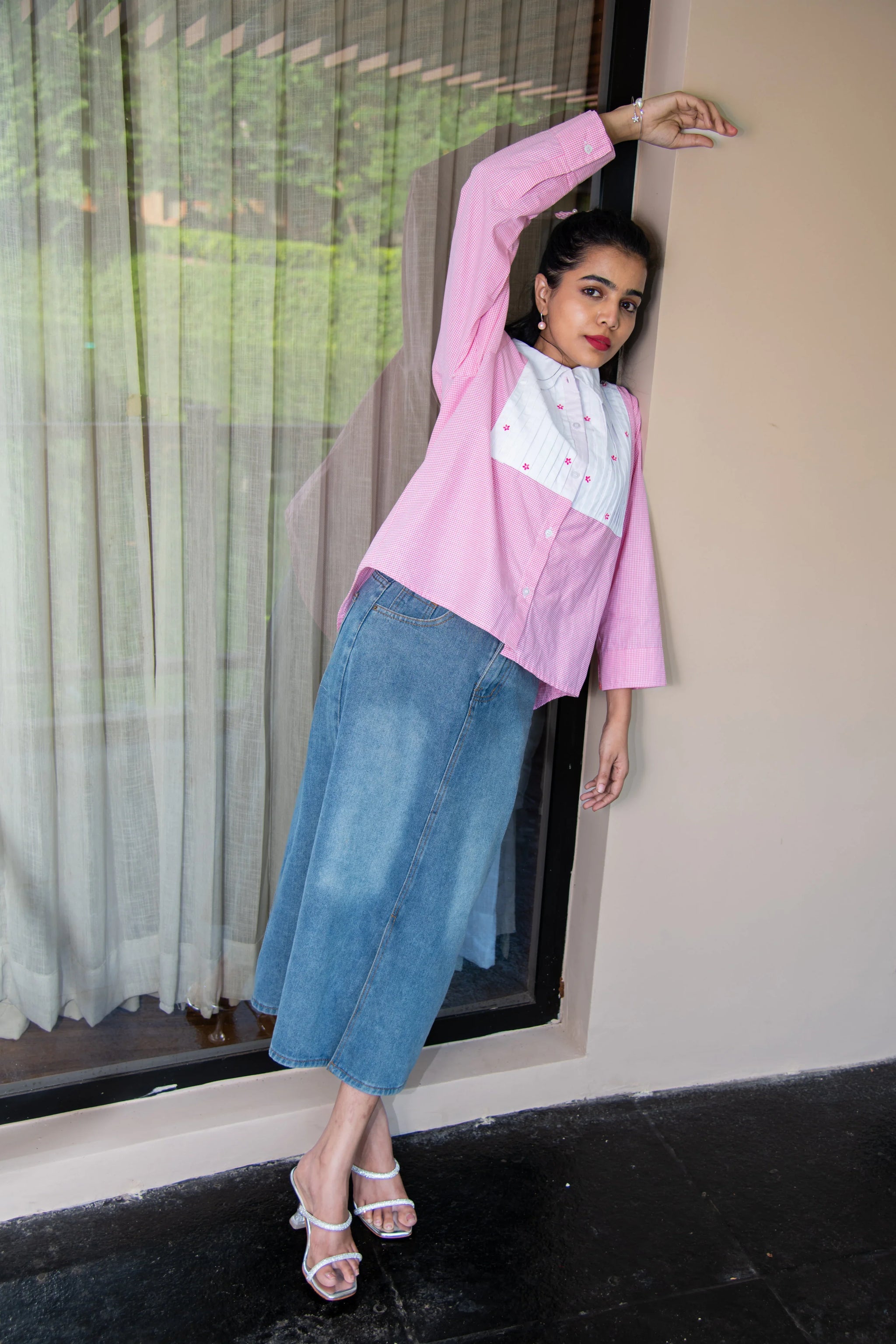Woman in pink and white shirt with embroidery, blue denim skirt, and heeled sandals posing outdoors