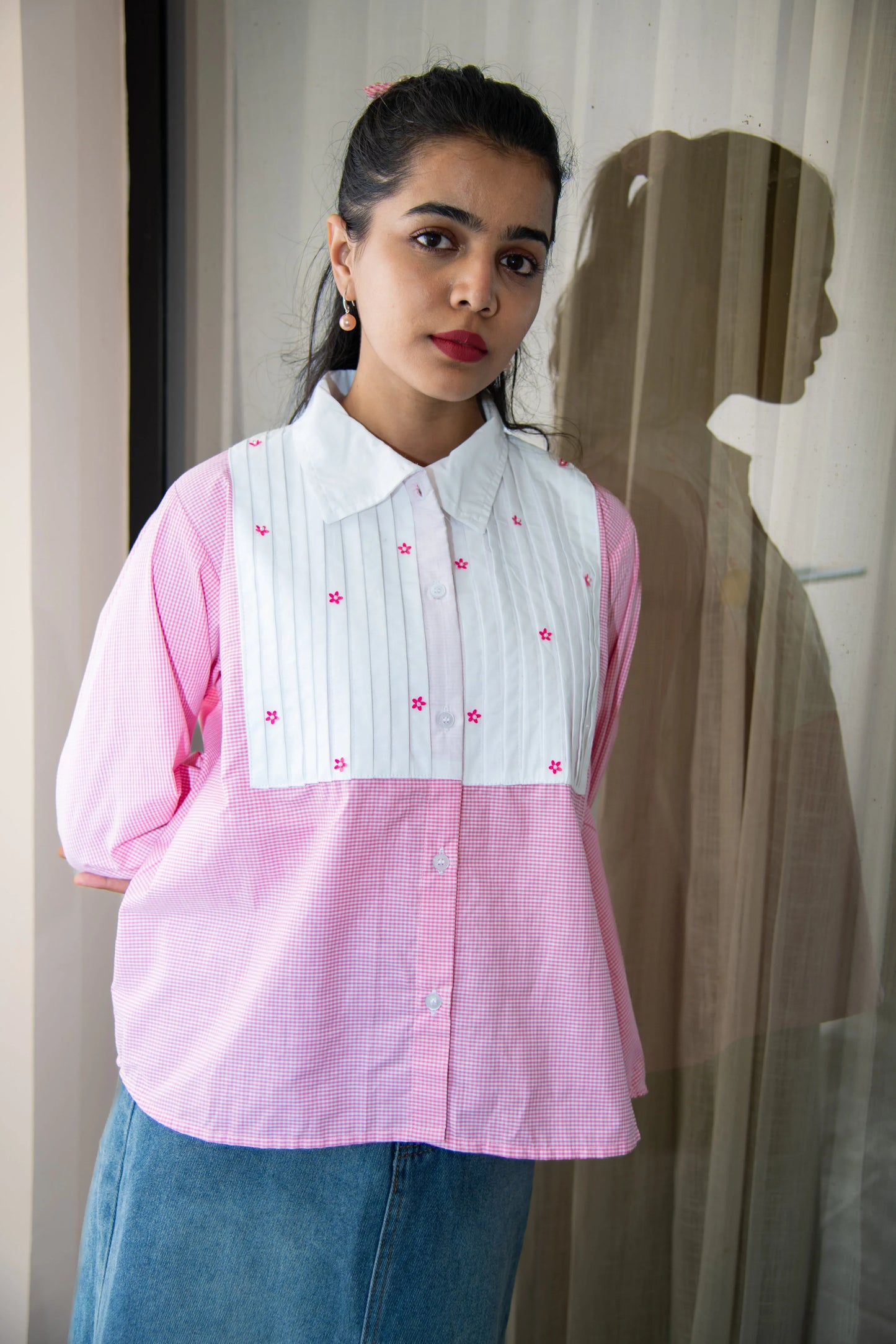 Woman wearing a pink checkered oversized shirt with white bib and floral embroidery