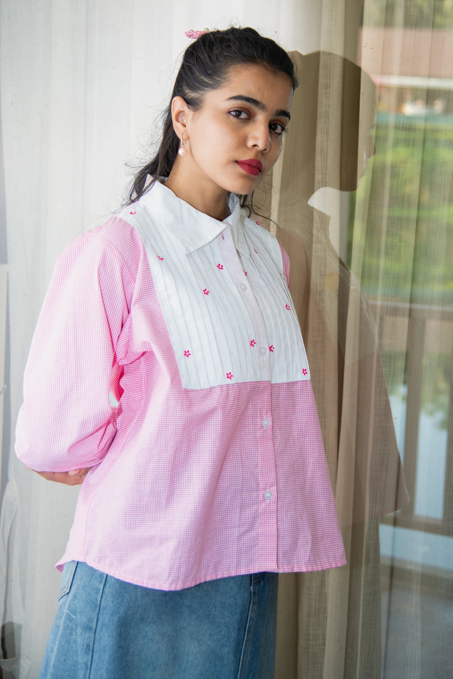Woman wearing a pink checkered shirt with white bib and floral embroidery, styled with denim skirt.