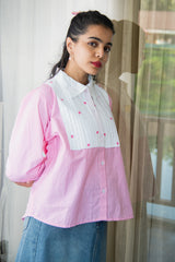 Woman wearing a pink checkered shirt with white bib and floral embroidery, styled with denim skirt.