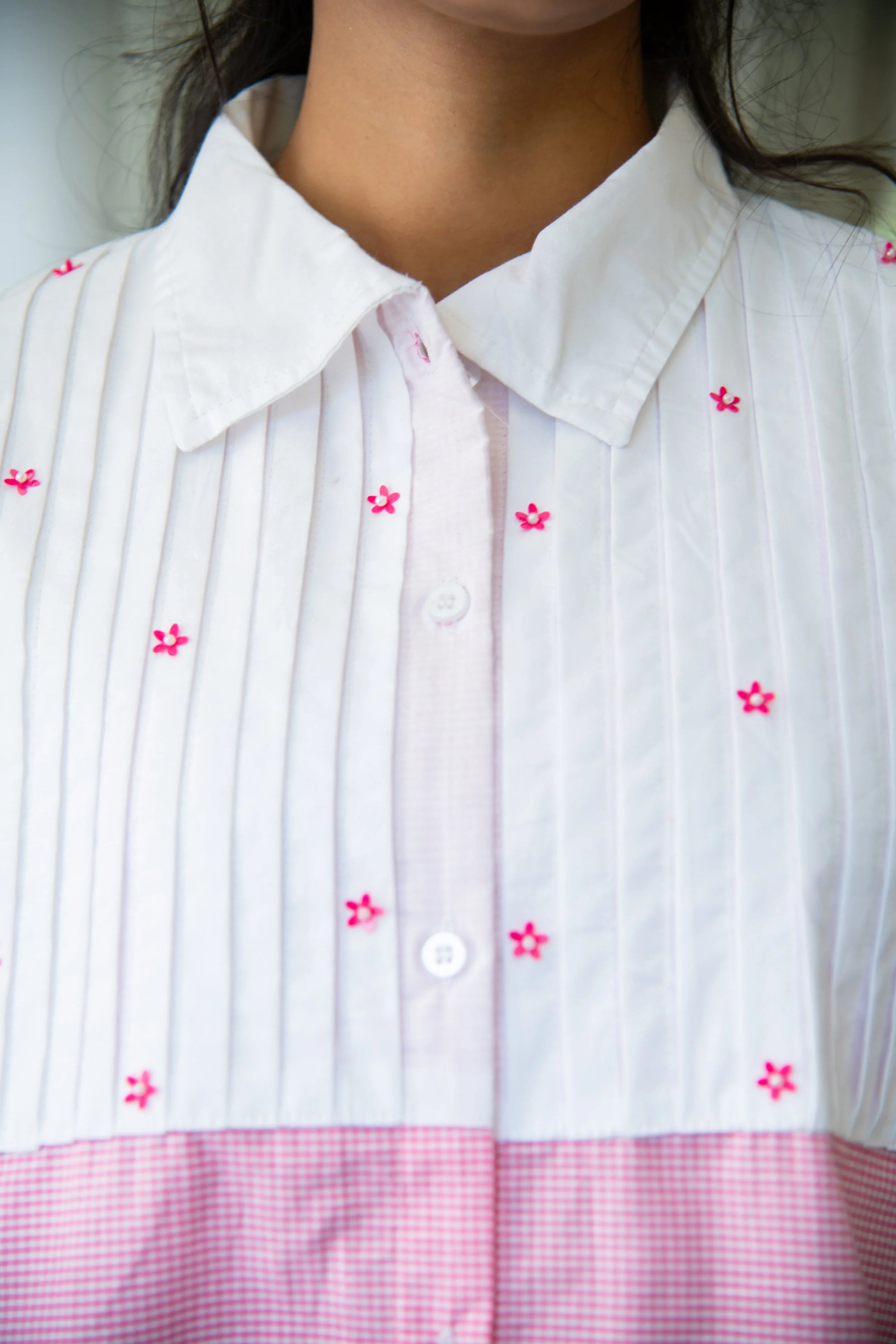 White collared dress with pink embroidered flowers and vertical pleats, close-up view