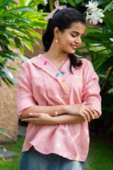 Woman in pink embroidered top with butterfly details, standing outdoors among green plants
