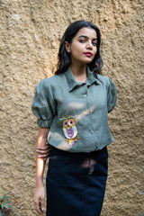 Woman wearing sage green puff sleeve shirt with owl patch, paired with black skirt