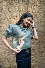 Woman wearing green puff sleeve shirt with beaded owl embroidery, casual outdoor style