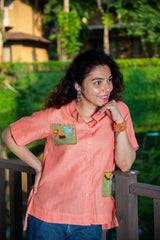 Woman in peach short-sleeve shirt with bird embroidery, standing outdoors on a balcony