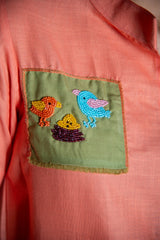 Peach shirt with green pocket featuring colorful beaded bird embroidery