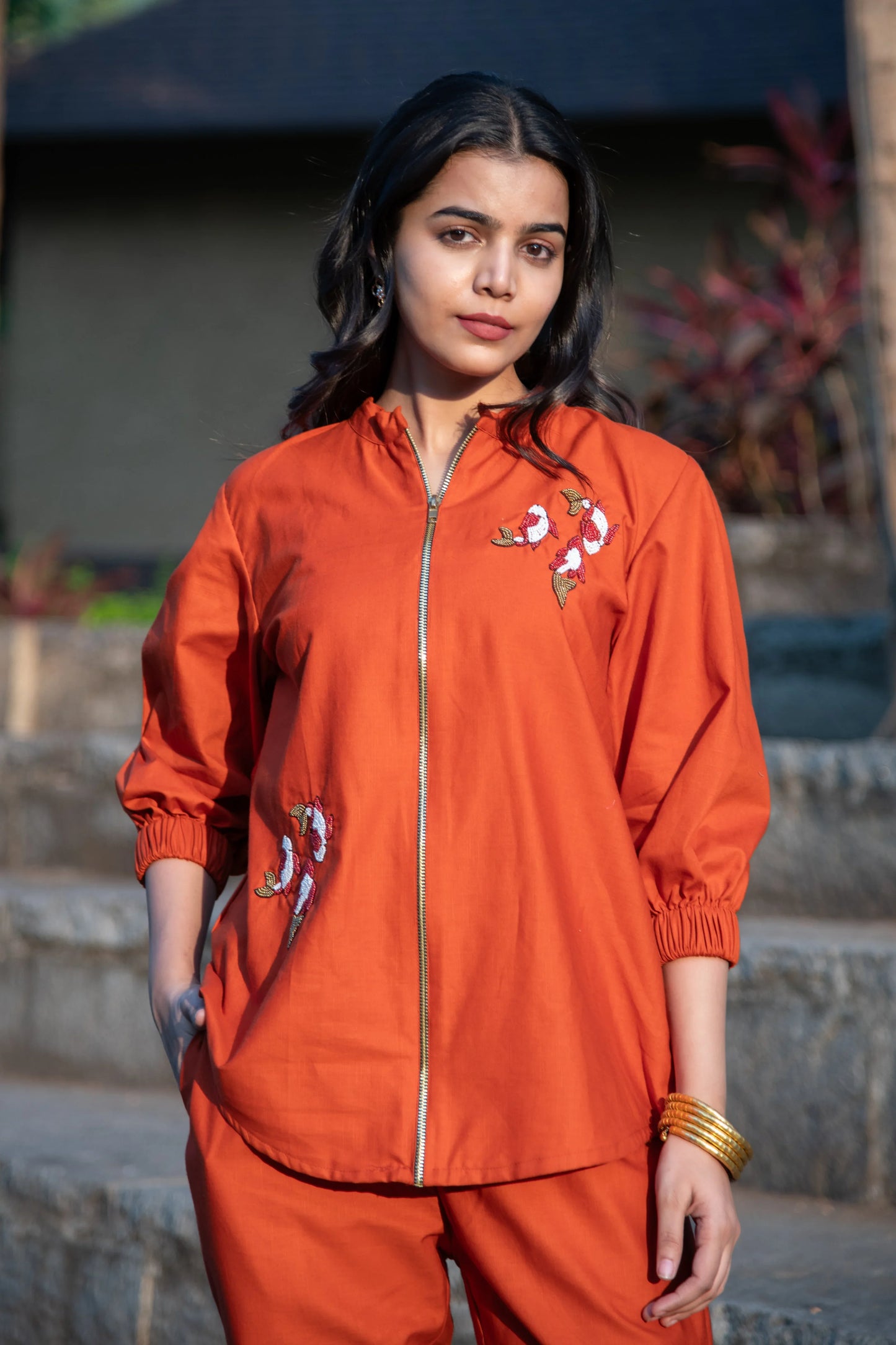Woman wearing an orange embroidered co-ord set with front zipper, outdoor setting