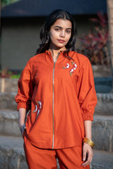 Woman wearing an orange embroidered co-ord set with front zipper, outdoor setting