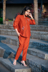 Woman wearing rust orange co-ord set with floral embroidery, standing on stone steps outdoors