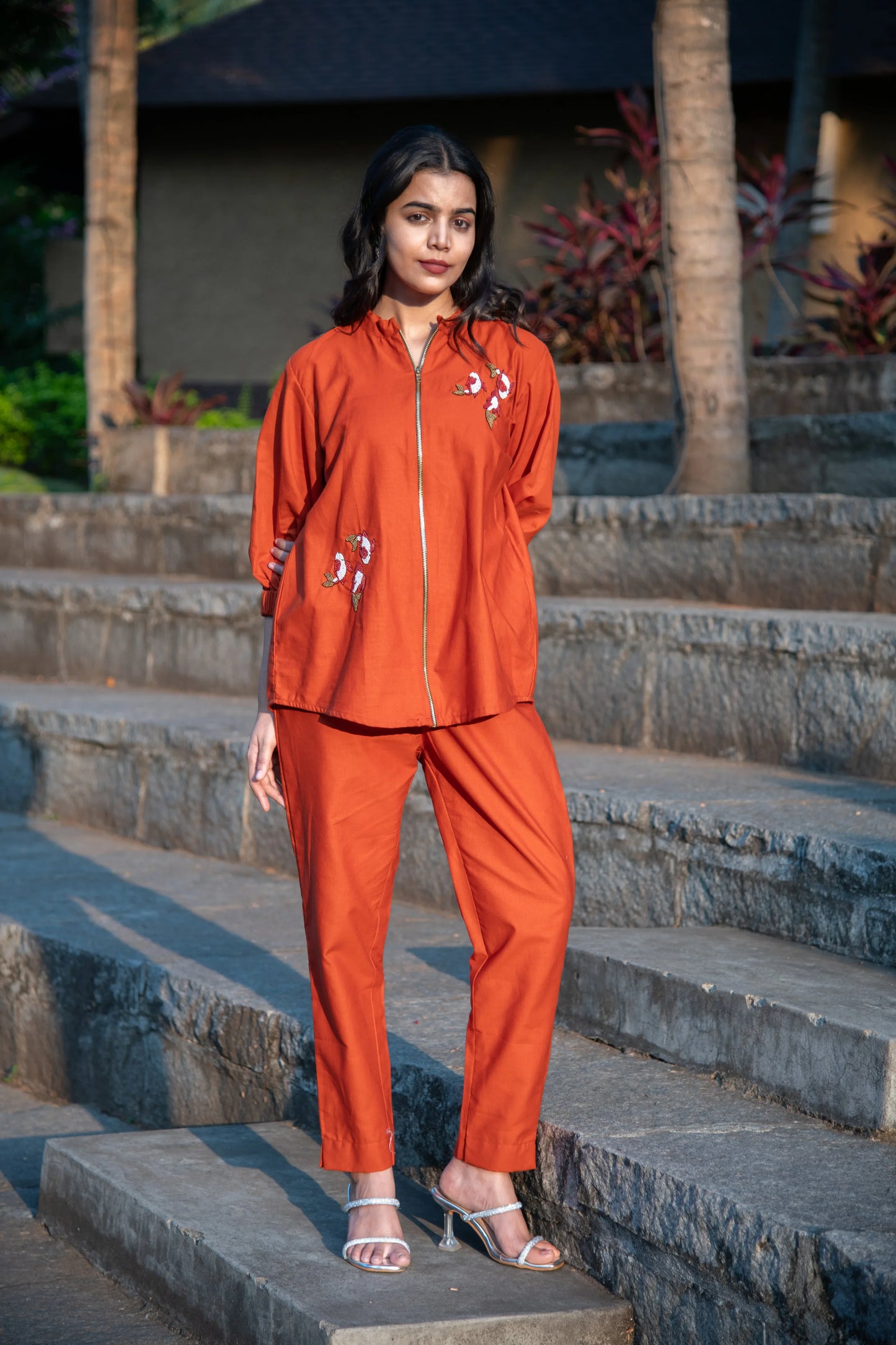 Woman wearing orange co-ord set with floral embroidery, posing outdoors on stone steps