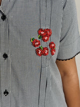 A close-up of a black and white gingham dress with a cluster of red beaded flower embellishments on the chest.
