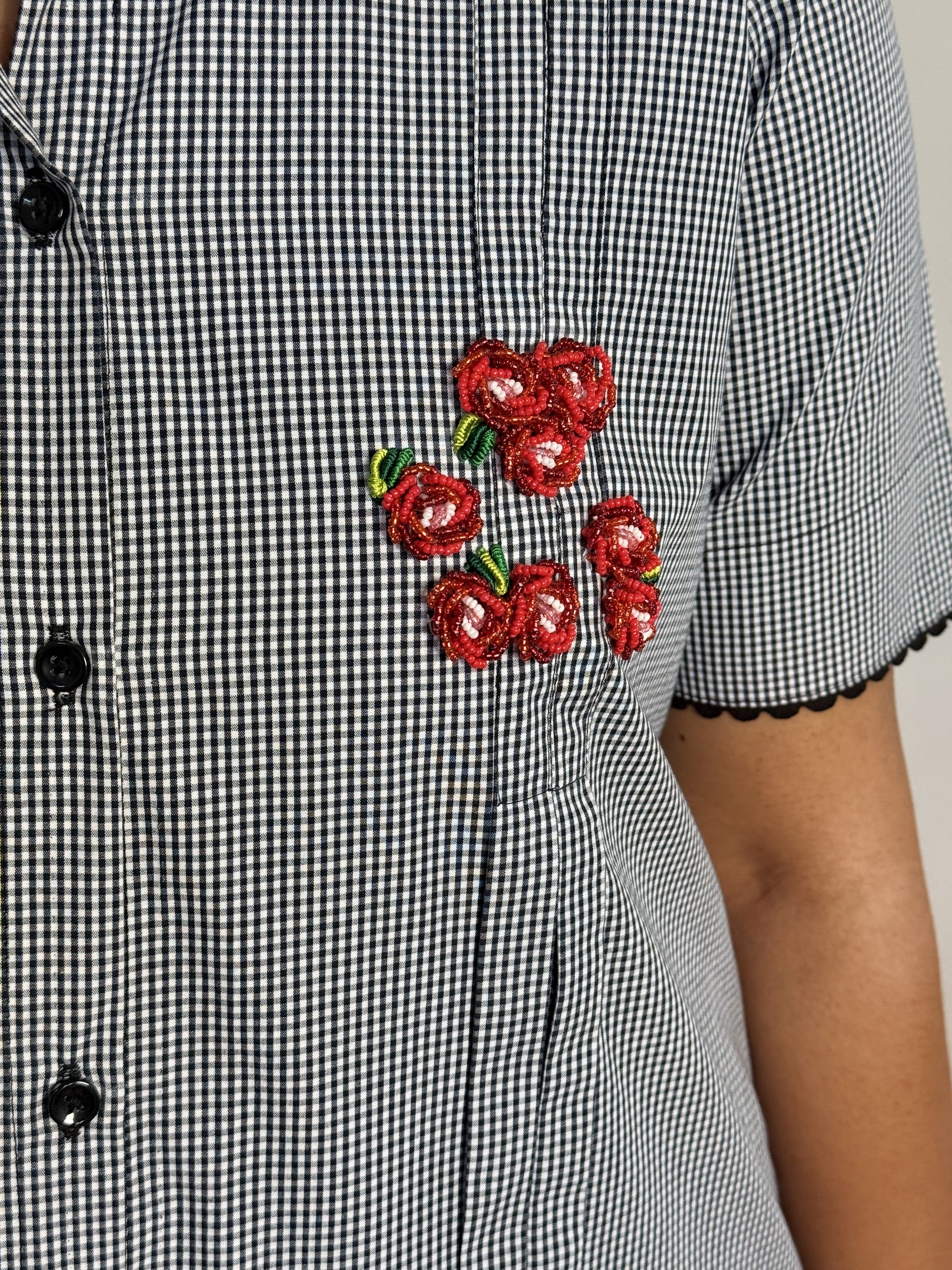 A close-up of a black and white gingham dress with a cluster of red beaded flower embellishments on the chest.