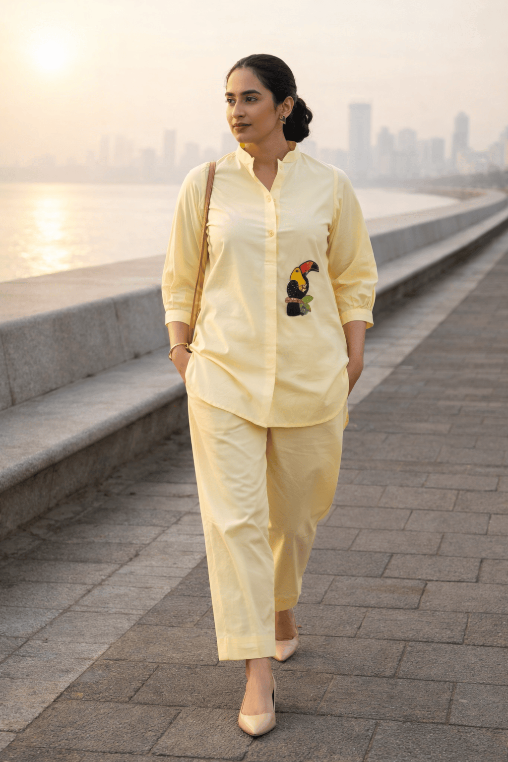 Yellow button-down shirt with toucan embroidery paired with matching pants, worn by woman near waterfront
