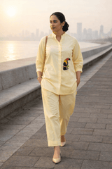 Yellow button-down shirt with toucan embroidery paired with matching pants, worn by woman near waterfront